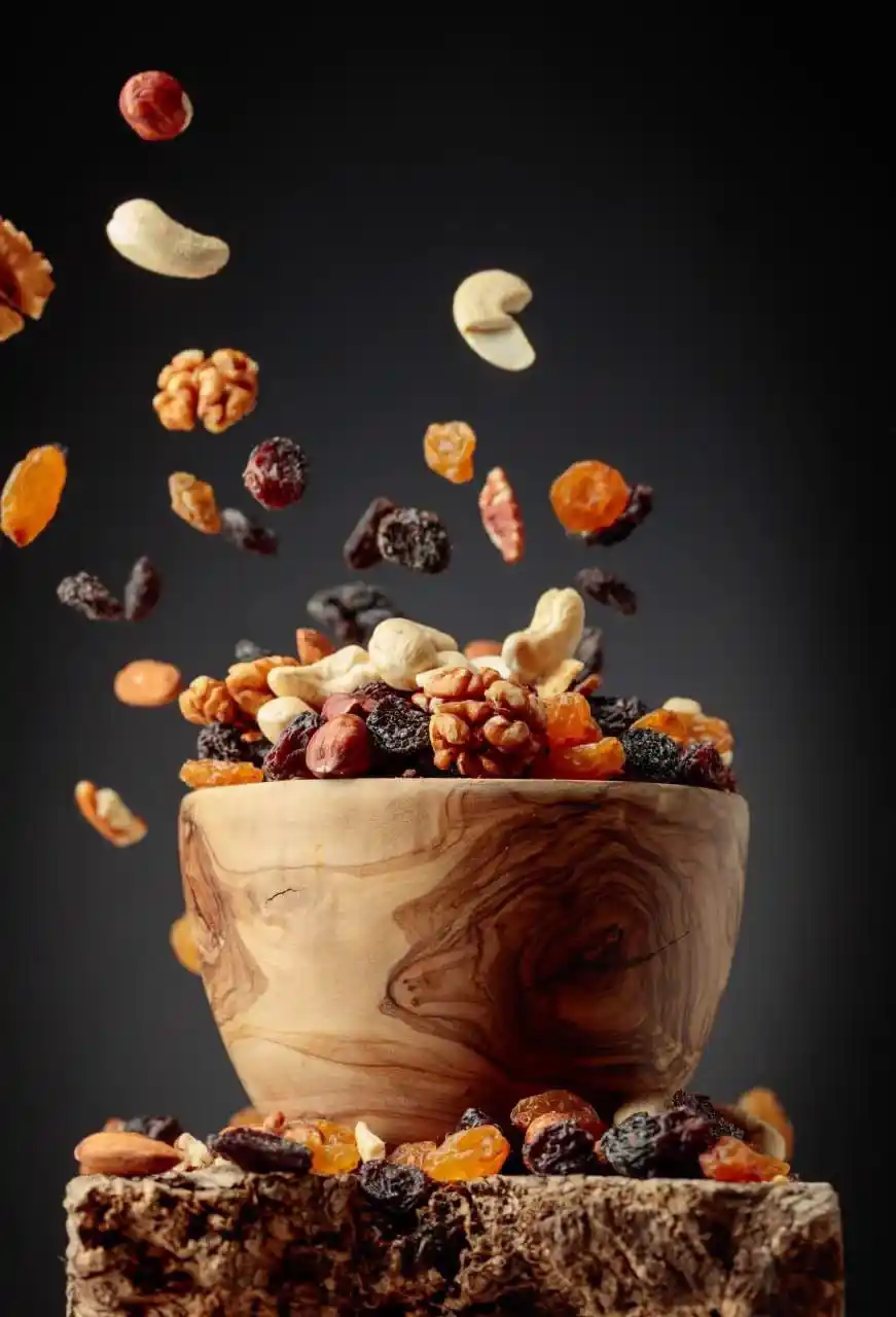 Mixed nuts and dried fruits falling into a wooden bowl